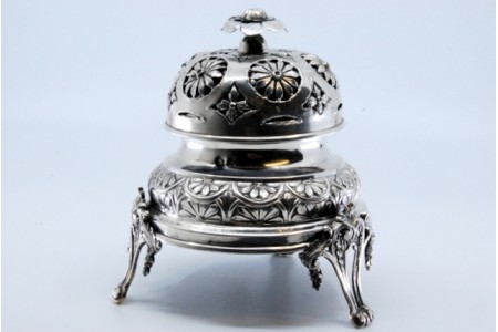  Campainha em prata com relevos florais, mecanismo no interior e assente sobre quatro pés.