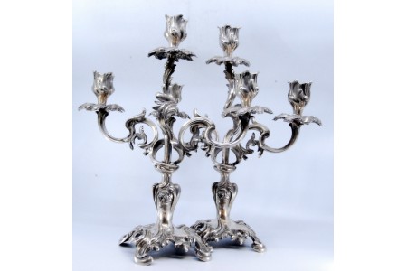 Candelabros em prata com três braços rameados e tulipas para as velas, apoiados em bases recortadas.