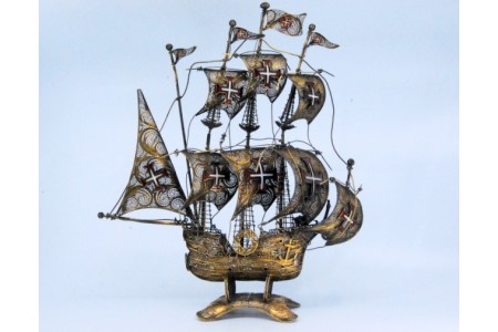 Caravela de prata filigrana com cruzes esmaltadas nas oito velas e mastros, assente sobre base recortada.