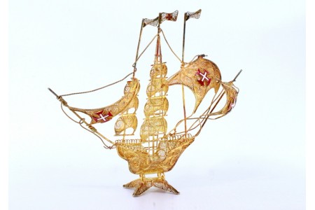 Caravela em prata filigrana com três mastros, cruzes esmaltadas nas velas e assente sobre base recortada.