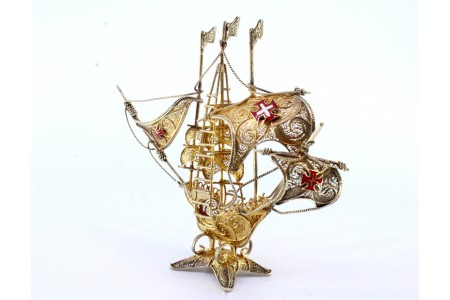 Caravela em prata filigrana dourada com cruzes esmaltadas nas velas e mastro assente sobre base recortada dividida em quatro.