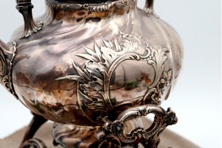 Chaleira em prata com relevos gomados e aplicações, trempe, corpo aspiralado, lamparina na base e assente em quatro pés alteados.