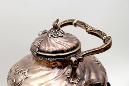 Chaleira em prata com relevos gomados e aplicações, trempe, corpo aspiralado.