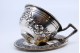  Chávena com pires em prata com motivos florais relevados e pega com aplicações.