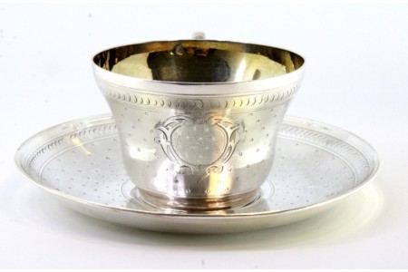 Chávena e pires em prata guilhochada envolvendo cartelas para monogramas e interior dourado.
