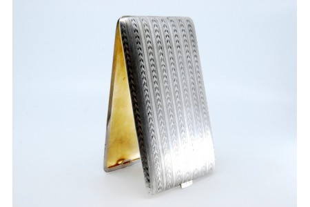 Cigarreira em prata com bandas espinhadas ao longo envolvendo cartela para para monograma, interior dourado e tampa basculante.