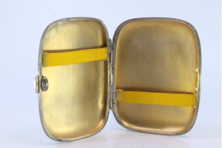 Cigarreira em prata guilhochada com bandas ao longo de forma curva e interior dourado.