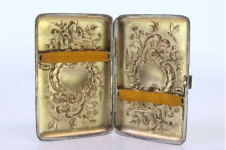 Cigarreira em prata com motivos florais relevados envolvendo cartelas para monogramas e tampa basculante.