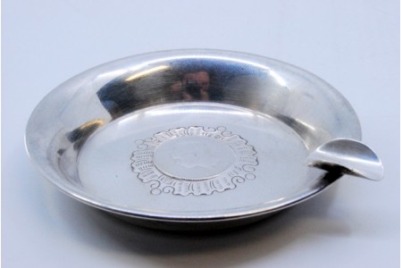 Cinzeiro em prata pequeno com relevo ao centro e moeda de 100 réis incrustada.