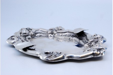 Cinzeiro em prata com relevos concheados, gravados no centro e dois suportes para cigarros.