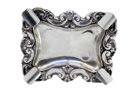 Cinzeiro em prata com relevos e aplicações, com quatro suportes para cigarros, e assente em quatro pés redondos.