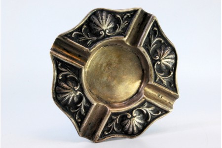 Cinzeiro em prata com relevos em forma de conchas e quatro apoios para cigarros.