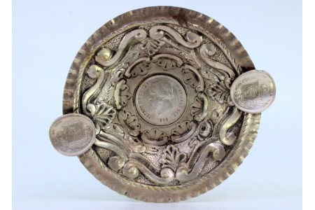  Cinzeiro em prata relevada envolvida por friso ondeado e moeda de mil reis ao centro, apoios para cigarros e argolas de fixação.