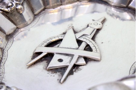 Cinzeiro em prata concheada com relevos, quatro suportes para cigarros e símbolo maçónico no centro.