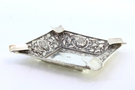 Cinzeiro em prata com motivos florais relevados, friso cordeado e quatro suportes para cigarros.