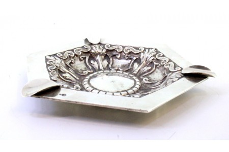 Cinzeiro em prata com relevos envolvendo cartela para monograma ao centro e três suportes para cigarros.