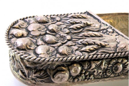 Cinzeiro em prata com forma de lata conserva com motivos florais revelados e assente em quatro pés retorcidos.