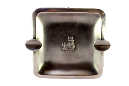 Cinzeiro em prata com relevos alusivos à torre de Belém no centro fosco, dois suportes para cigarros e assente em quatro pés.