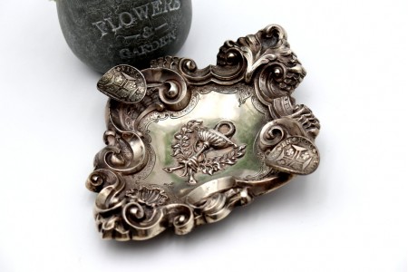 Cinzeiro em prata com relevos concheados e símbolo ao centro