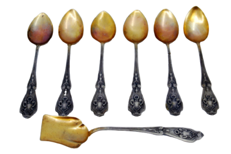 Conjunto de seis colheres de café e pá de açúcar em prata com conchas douradas e cabos relevados.