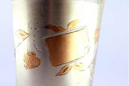 Copo em prata fosca com motivos florais gravados e realçados a dourado envolvendo cartela para monograma, interior dourado.