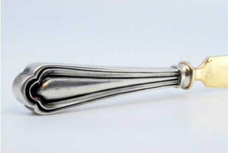 Faca para queijo em prata dourada com frisos ao longo do cabo.