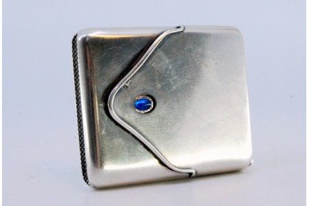 Fosforeira em prata em forma de envelope com aplicação de cabochão azul no centro.