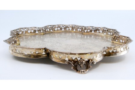 Bandeja com gradinha em forma lobolada e fundo gravado com motivos florais, assente sobre três pés recortados.