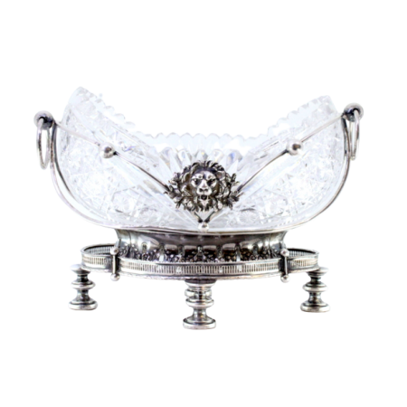 Fruteira em prata com alma em vidro lapidado estrutura com mascarões relevados e aplicações assente em base em gradinha e quatro pés altos em forma circular.