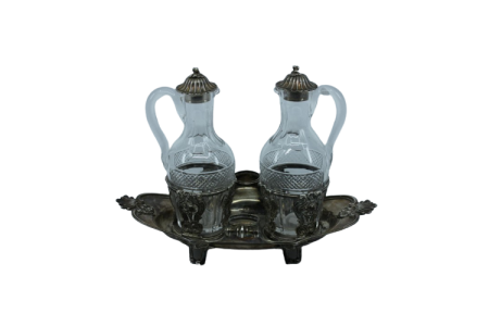 Galheteiro com estrutura em prata com motivos vegetalistas, duas galhetas em vidro lapidado e pomos nas tampas.