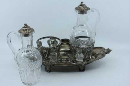 Galheteiro com estrutura em prata com motivos vegetalistas, duas galhetas em vidro lapidado e pomos nas tampas.