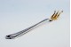 .Garfo de servir acepipes em prata com três dentes dourados e frisos ao longo do cabo.