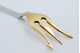 .Garfo de servir acepipes em prata com três dentes dourados e frisos ao longo do cabo.