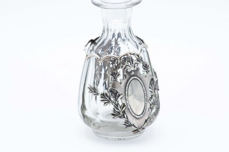 Garrafa para  licor em vidro lapidado com aplicações de colunas em prata, flores e ramos suspensos envolvendo cartela para monograma.