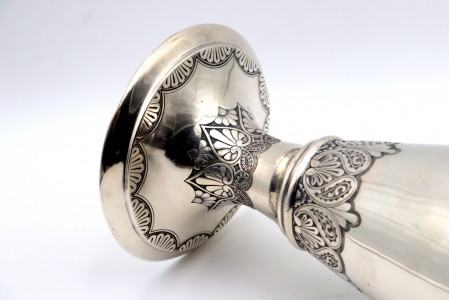 Jarra de prata alta com motivos florais relevados e gravados na base circular.