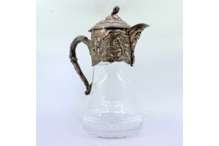 Jarro de vinho com corpo em vidro liso e aplicação em prata relevada, com motivos florais e pomo na tampa em forma de flor.