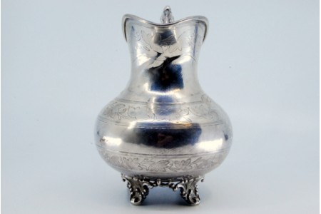 Jarro de água em prata com motivos vegetalistas gravados e assente em quatro pés relevados.