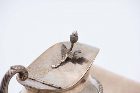 Leiteira em prata de asa perdida relevada, friso na envolvência e pomo na tampa basculante em forma de bolota.