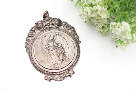 Medalha em prata com figura de anjo da guarda e criança, bordos em alto relevo