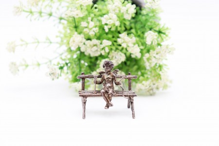 Miniatura em prata de Cupido sentado em banco de jardim