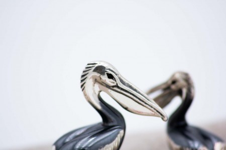 Par de pelicanos em prata nielada em posição de sentados.