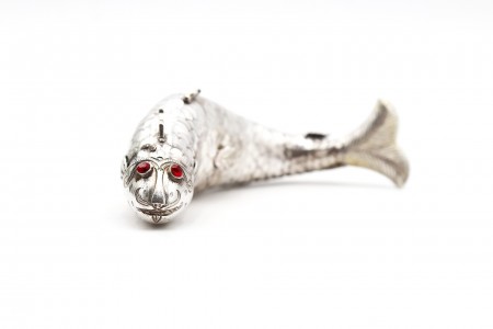 Peixe articulado em prata relevada com pedras vermelhas nos olhos.