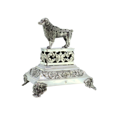 Paliteiro em prata com cão sobre plinto recortado em base relevada com volutas e assente sobre quatro pés relevados.