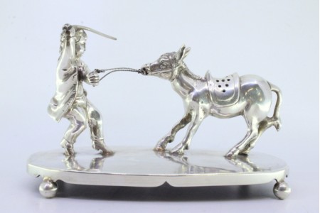 Paliteiro em prata com criança puxando burro assente em base lisa com quatro pés redondos.