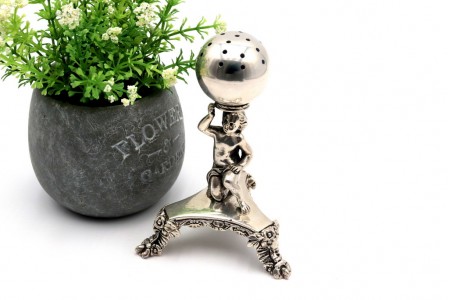 Paliteiro em prata com menino segurando esfera sobre pedestal relevado de formato trípodo e assente em três pés com  aplicações.