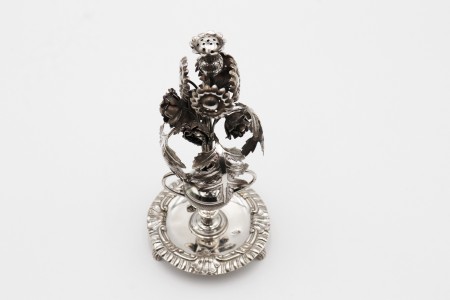 Paliteiro em prata com acanteiro de vulto perfeito, flores e folhas sobre jarra com duas asas e frisos.