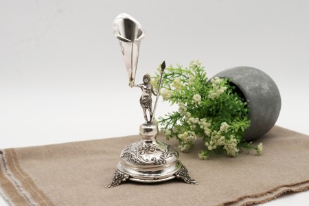  Paliteiro em prata com representação de pajem com lança, caliçe em forma de jarro (flor) assente em base circular em alto relevo e três pés relevados.