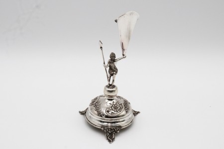  Paliteiro em prata com representação de pajem com lança, caliçe em forma de jarro (flor) assente em base circular em alto relevo e três pés relevados.