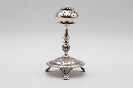 Paliteiro em prata em forma de morango assente em base circular adornada com motivos vegetalistas e três pés em forma de garras.