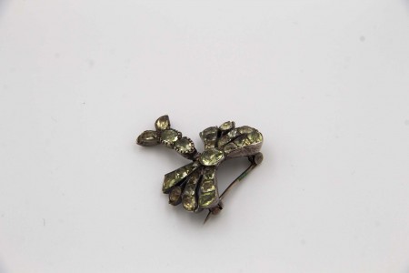 Pregadeira de prata em forma de laço com pingente articulados e crisólitas aplicadas.